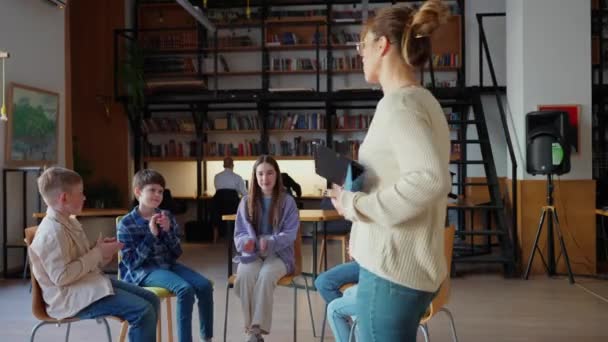 Позитивні Діти Плескають Вчителем Сидячи Колі Стільцях Шкільній Бібліотеці — стокове відео