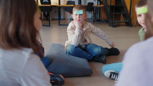 図書館の床の円に座っている額に紙を持っているか推測する高価な子供のゲーム — ストック動画