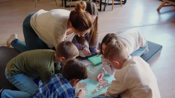 真剣な子供たちと教師たちは図書館の床に座っている世界地図を見る — ストック動画