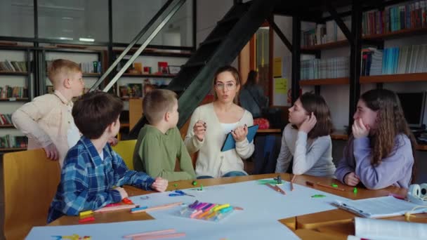 集中した教師が図書館でプラスチックの図面を描き 成形している子供たちと話す — ストック動画