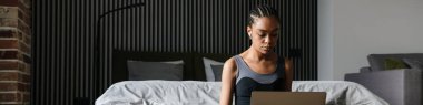 Healthy young fit african sportswoman using laptop computer while sitting on a fitness mat in the bedroom