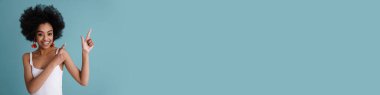 Mutlu Afrikalı Amerikalı kız gülümsüyor ve mavi arka planda tek başına parmaklarını havaya kaldırıyor.