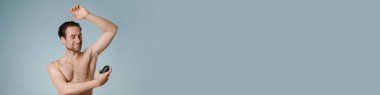 Yakışıklı, gülümseyen çıplak adam mavi arka planda izole edilmiş deodorant püskürtüyor.