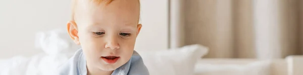 家でベッドで遊んでいる間にタブレットコンピュータを見てブロンドの赤ちゃん男の子を喜ばせます — ストック写真