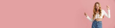 Mutlu güzel kız dans ediyor ve kutluyor pembe arka planda tek başına duruyor.