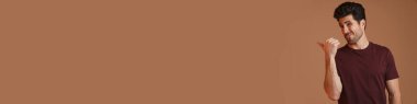 Kafası karışmış erkek pozu veriyor ve bej arka planda izole edilmiş bir şekilde parmağını işaret ediyor.