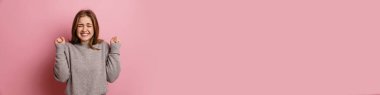 Ginger, heyecanlı genç kadın gülümserken pembe arka planda izole edilmiş kazanan jestler yapıyor.