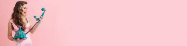 Pembe arka planda izole edilmiş retro telefonlu elbise giyen genç bir kadın.