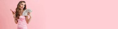 Pembe elbiseli, uzun sarı saçlı, pembe duvarda duran genç beyaz kadın Barbie.