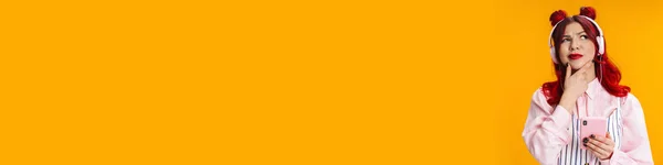 黄色の背景に隔離されたヘッドフォンと携帯電話で音楽を聞く赤い髪のブルーガール — ストック写真