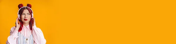 黄色の背景に隔離された見たヘッドフォンの不快な赤毛の少女 — ストック写真