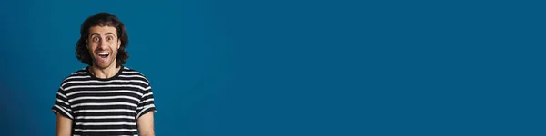 Возбужденный Брюнетка Мужчина Полосатой Футболке Восклицает Камеру Изолированы Синем Фоне — стоковое фото