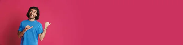 Возбужденная Брюнетка Мужчина Указывая Пальцами Сторону Улыбаясь Изолированы Розовом Фоне — стоковое фото
