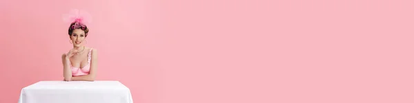 Молодая Женщина Бигуди Улыбается Камеру Сидя Столом Изолированы Розовом Фоне — стоковое фото