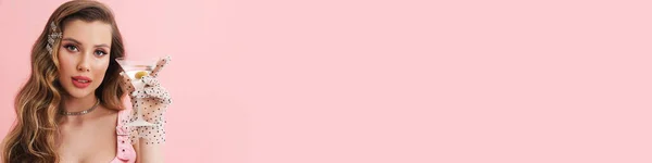 年轻的白人女人戴着手套 喝着鸡尾酒 看着被粉色背景隔离的相机 — 图库照片