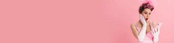 Удивлена Женщина Бигуди Восклицает Использовании Мобильного Телефона Изолированы Розовом Фоне — стоковое фото