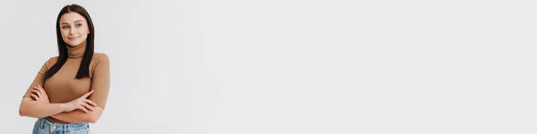 Счастливая молодая брюнетка белая женщина в повседневной одежде стоя на белом фоне, глядя в сторону, руки сложены