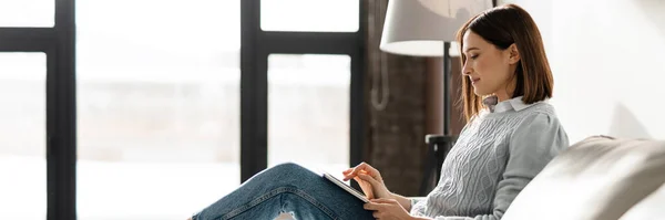 stock image Smiling middle aged woman using digital tablet while relaxing on a couch at home