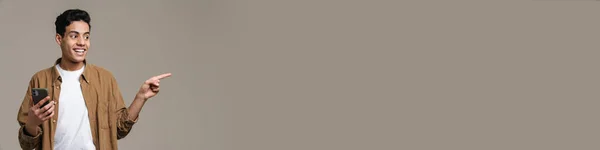 Улыбающийся Юный Брюнетка Футболке Стоящий Фоне Серой Стены Держа Мобильный — стоковое фото