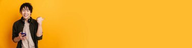 Sarı arka planda dururken gülümseyen Asyalı genç adam başarıyı kutluyor.