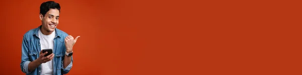Улыбающийся Человек Указывая Пальцем Сторону Используя Мобильный Телефон Красном Фоне — стоковое фото