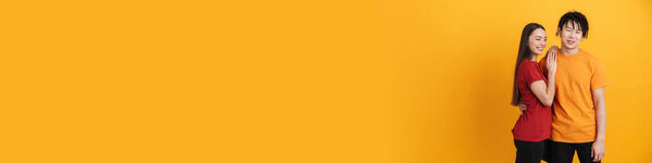 Young multiracial couple smiling and hugging while posing on camera isolated over yellow wall