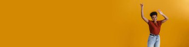 Happy casually dressed young african woman standing over yellow wall background, dancing