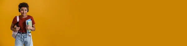 Улыбающаяся Чёрная Женщина Наушниках Позирует Рюкзаком Тетрадками Жёлтом Фоне — стоковое фото