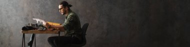 Sakallı, odaklı bir zanaatkar atölyede deriyle çalışırken notlar yazıyor.