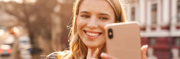 Sorrindo Jovem Loira Tomando Uma Selfie Enquanto Caminha Uma Rua — Fotografia de Stock