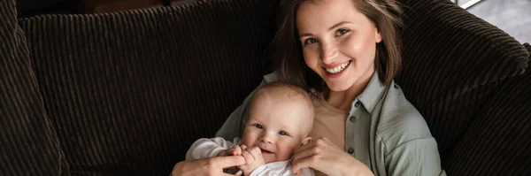 幸せな母親と彼女の赤ちゃんの男の子は自宅のソファーで抱っこ — ストック写真