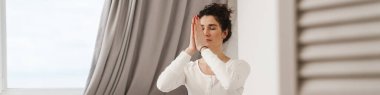 Düşünceli kadın, aydınlık odada yatakta otururken gözleri kapalı meditasyon yapıyor.