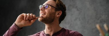 Düşünceli adam gülümsüyor ve stüdyoda masada otururken çenesine kalem tutuyor.