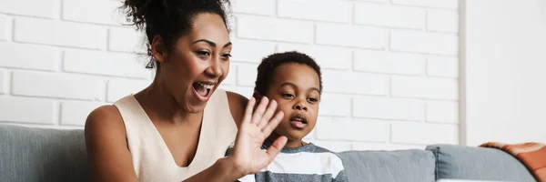 stock image Black happy mother and son gesturing while using laptop at home