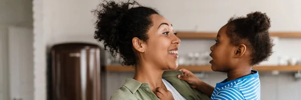 stock image Black happy mother laughing while holding her daughter at home kitchen