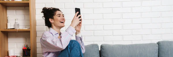 Wanita Keriting Bahagia Duduk Dengan Kaki Sofa Dan Melihat Telepon — Stok Foto