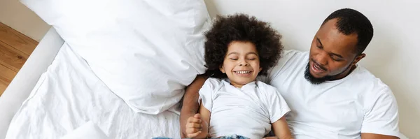 Black father and son laughing while making fun in bed at home