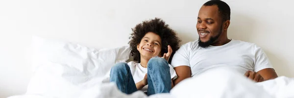 Black father and son laughing while lying in bed at home