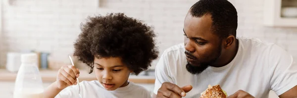 Black father and son having breakfast while sitting at table in home kitchen