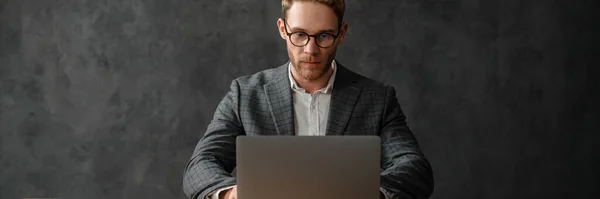 一个穿着夹克和衬衫的男人坐在工作室里笔记本电脑前的桌子前 — 图库照片