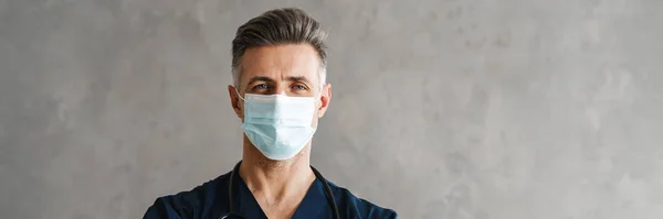 屋内に立つ保護医療用マスクで自信を持って中年男性医師 — ストック写真