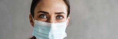 Medikal koruyucu maske takan orta yaşlı esmer kadın doktor içeride kameraya bakıyor.