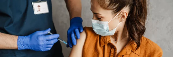 彼のキャビネットの医者によってコビド19からワクチン接種を受ける保護マスクを着用している女性患者 — ストック写真