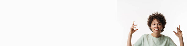 Молодая кудрявая брюнетка улыбается с поднятыми руками на белом фоне