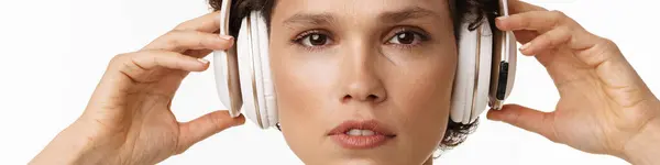 年轻的卷曲黑发女子 带着耳机在白色背景下听音乐 — 图库照片
