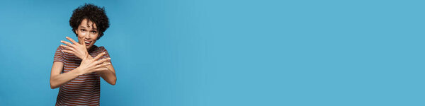 Молодая кудрявая брюнетка женщина жестом и улыбаясь в камеру изолированы на синем фоне