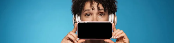 若いです巻きブルネット女性身に着けているヘッドフォンショー携帯電話隔離された青白の背景 — ストック写真