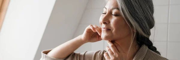 stock image Mature grey woman smiling while getting facial massage in bathroom at home