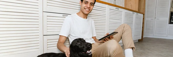 Sorrindo Hispânico Jovem Acariciando Seu Cão Enquanto Sentado Chão Cozinha — Fotografia de Stock