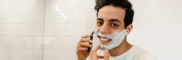 Sonriente Joven Hispano Afeitándose Cara Parado Frente Espejo Dentro — Foto de Stock